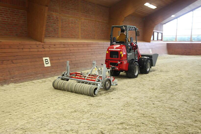 Weidemann Hoftrac 1160e in einer Reithalle mit Leichtgutschaufel und Reitplatz- und Bahnenplaner